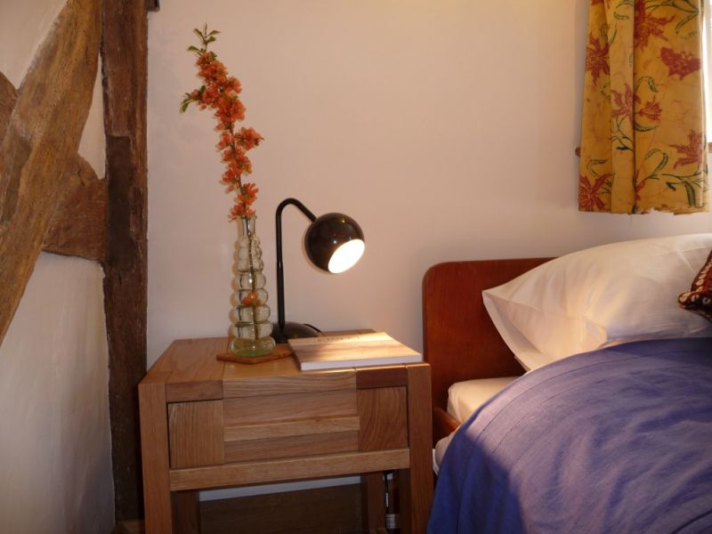 A bedside table with a curved black lamp and a vase of orange flowers next to a bed with blue covers.